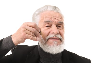 Photo of Senior man applying serum onto his beard on white background