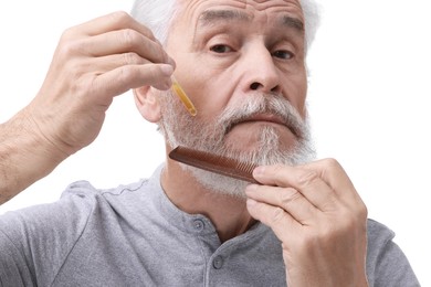 Photo of Senior man with comb applying oil onto his beard on white background