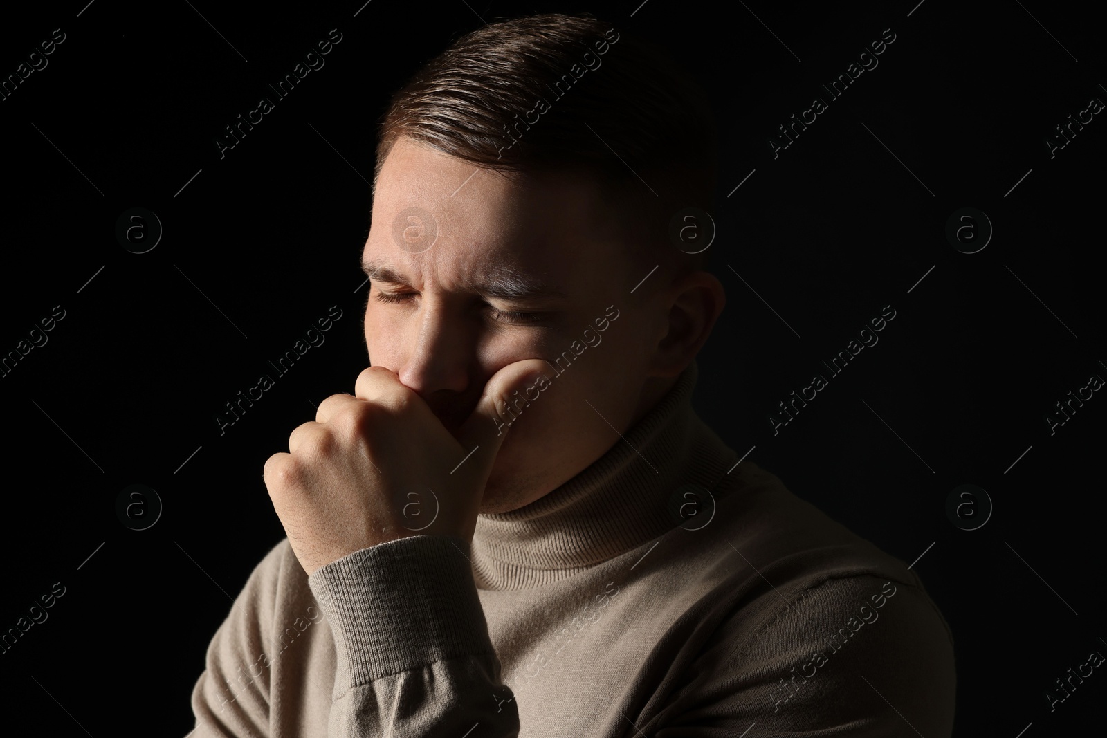 Photo of Distressed young man crying on black background