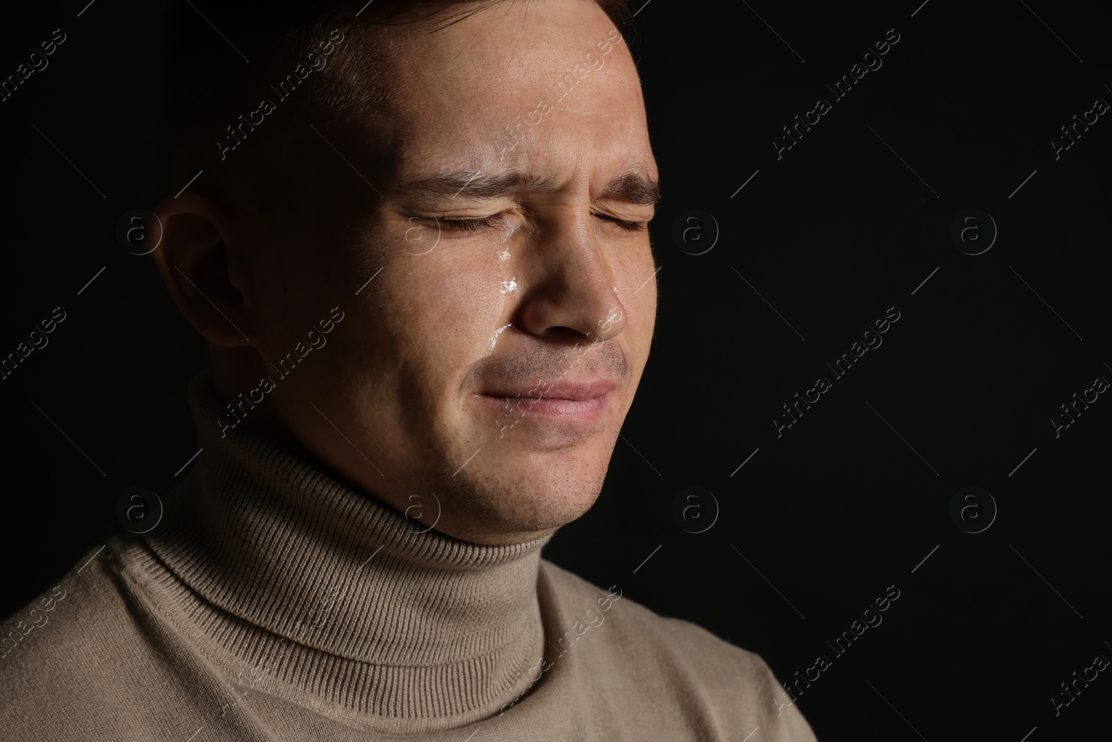 Photo of Distressed young man crying on black background