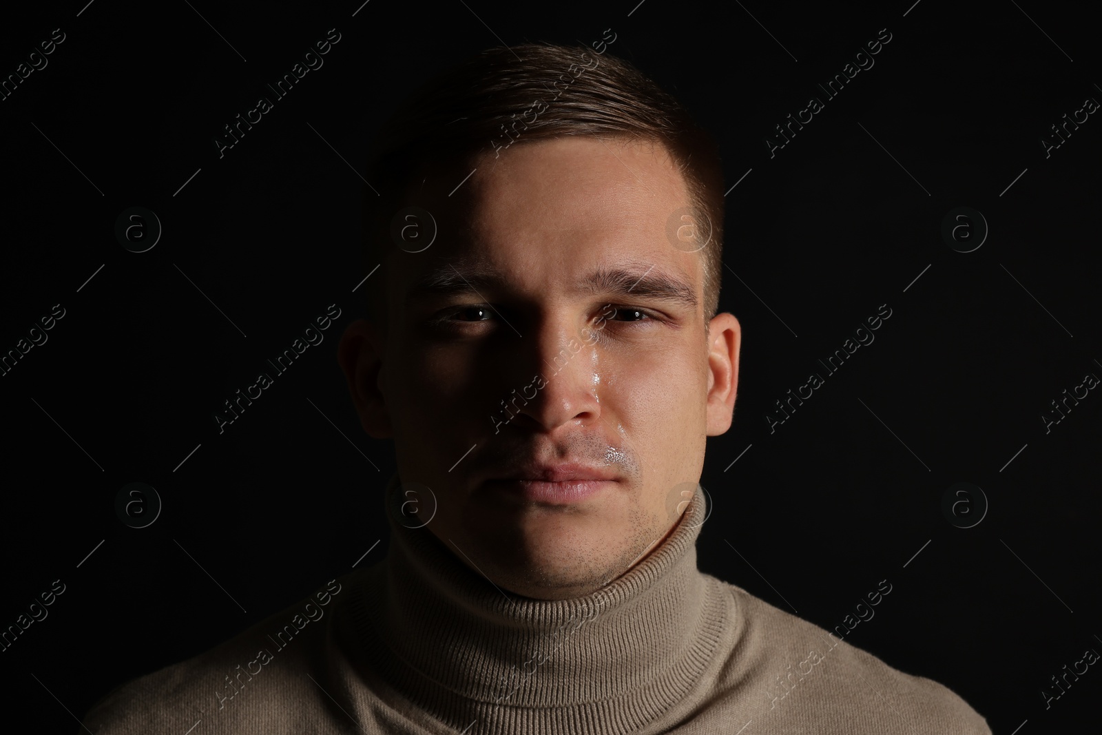 Photo of Distressed young man crying on black background