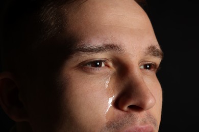 Photo of Distressed young man crying on black background, closeup