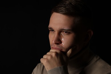 Photo of Distressed young man crying on black background. Space for text