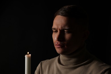 Photo of Man with burning candle crying on black background. Space for text