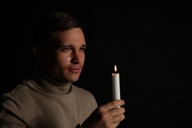 Man with burning candle crying on black background. Space for text