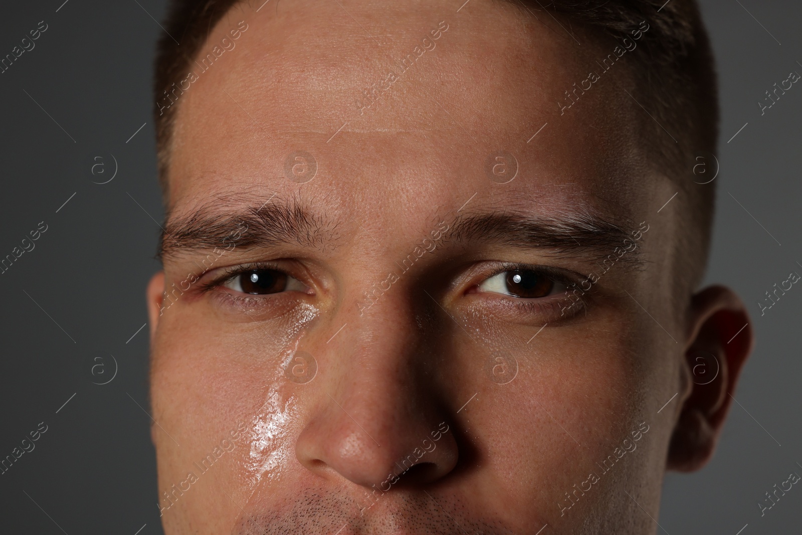 Photo of Distressed young man crying on grey background, closeup