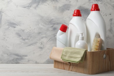 Photo of Eco-friendly cleaning products and supplies in crate on light wooden table, space for text