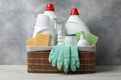 Photo of Eco-friendly cleaning products and supplies in wicker basket on light wooden table