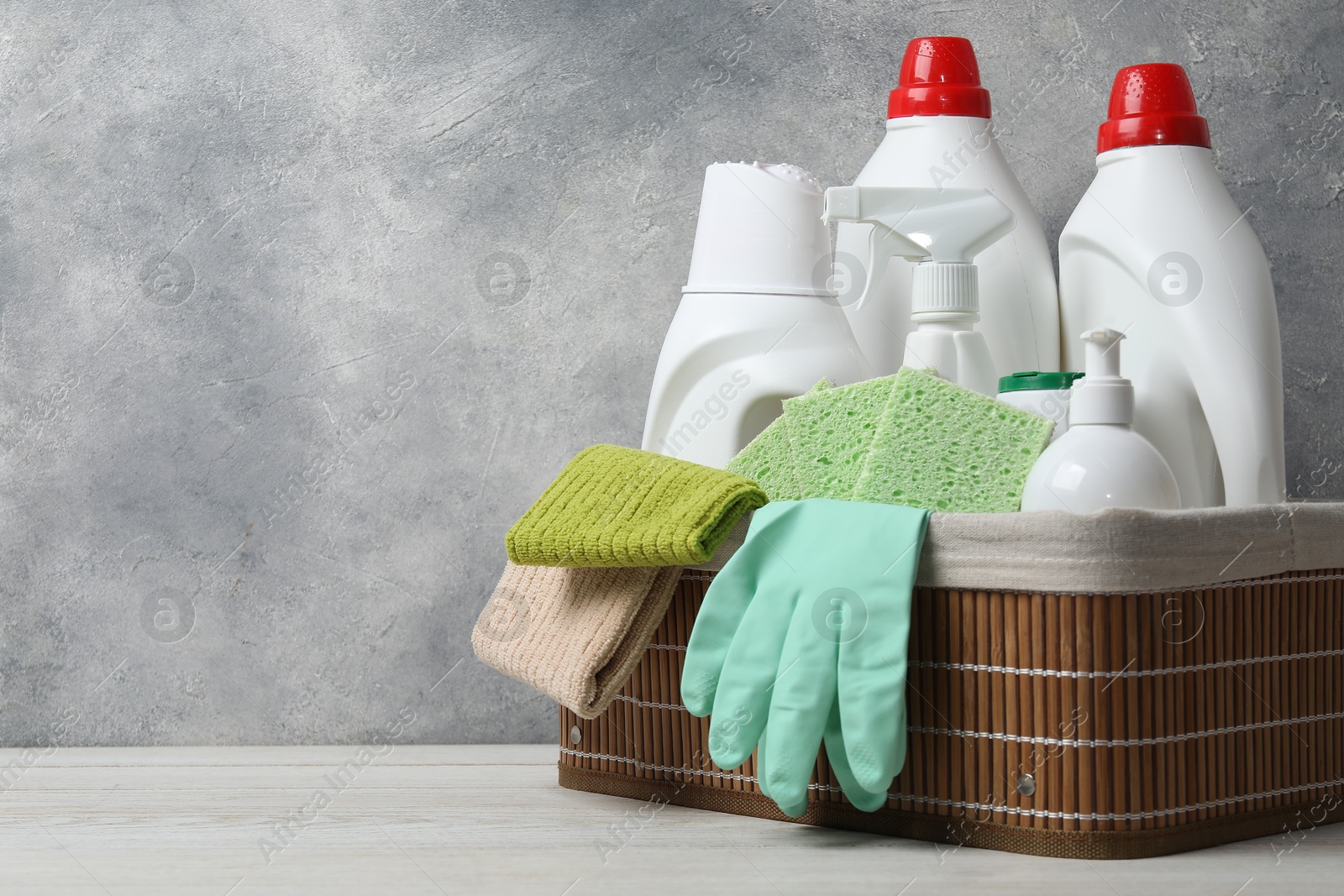 Photo of Eco-friendly cleaning products and supplies in wicker basket on light wooden table, space for text