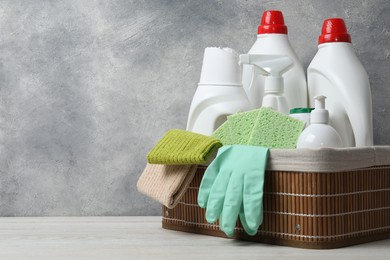 Photo of Eco-friendly cleaning products and supplies in wicker basket on light wooden table, space for text