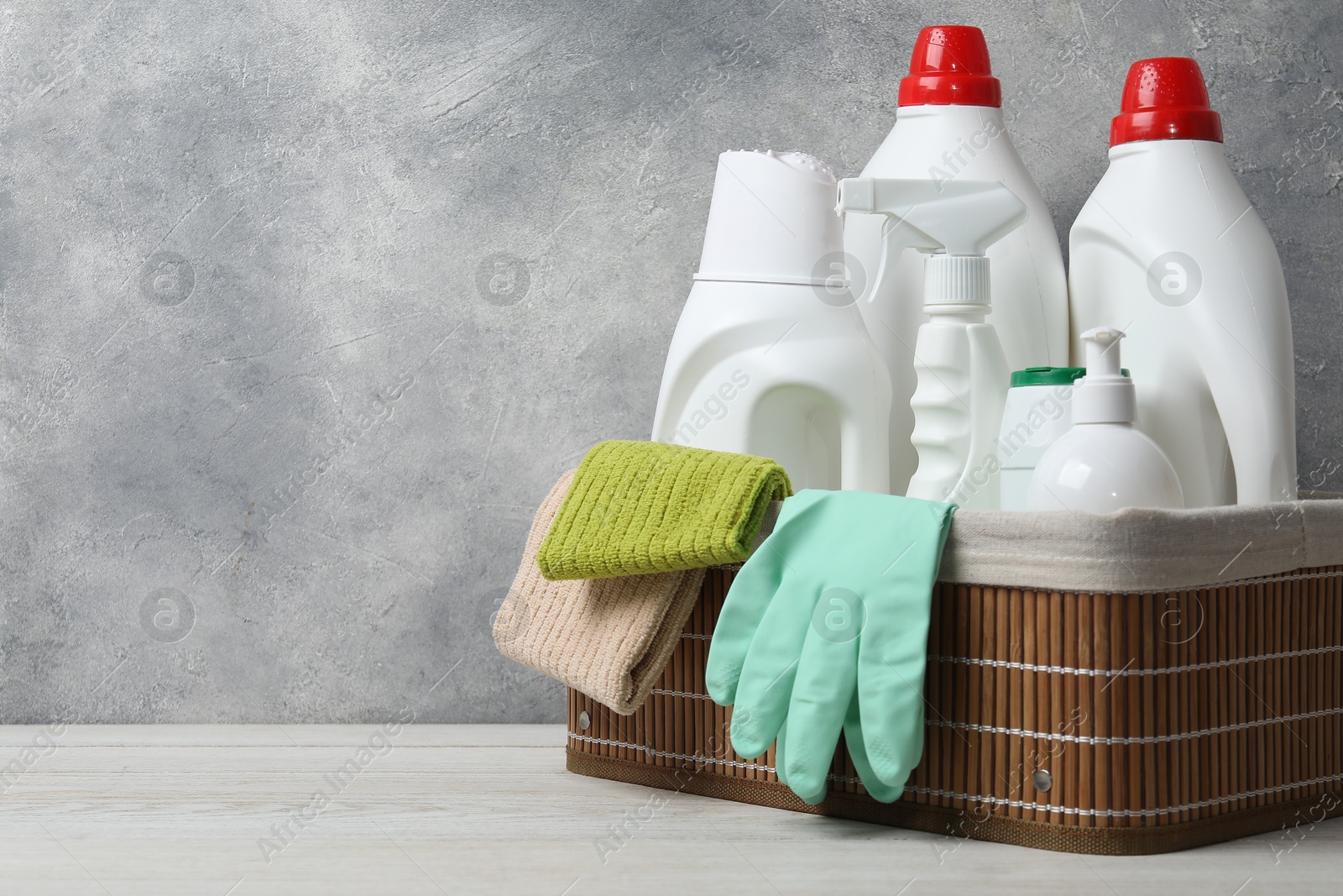 Photo of Eco-friendly cleaning products and supplies in wicker basket on light wooden table, space for text