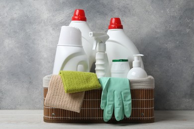 Photo of Eco-friendly cleaning products and supplies in wicker basket on light wooden table