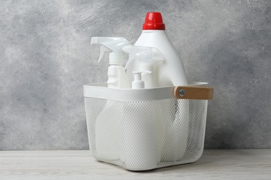 Photo of Different cleaning products in basket on light wooden table