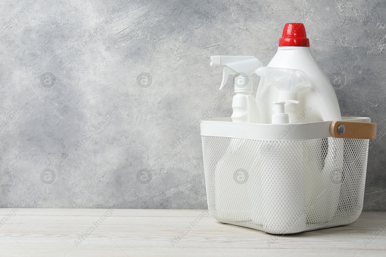 Photo of Different cleaning products in basket on light wooden background, space for text