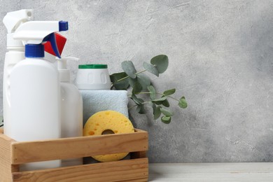 Photo of Eco-friendly cleaning products, supplies and eucalyptus branches in crate on light wooden table, space for text