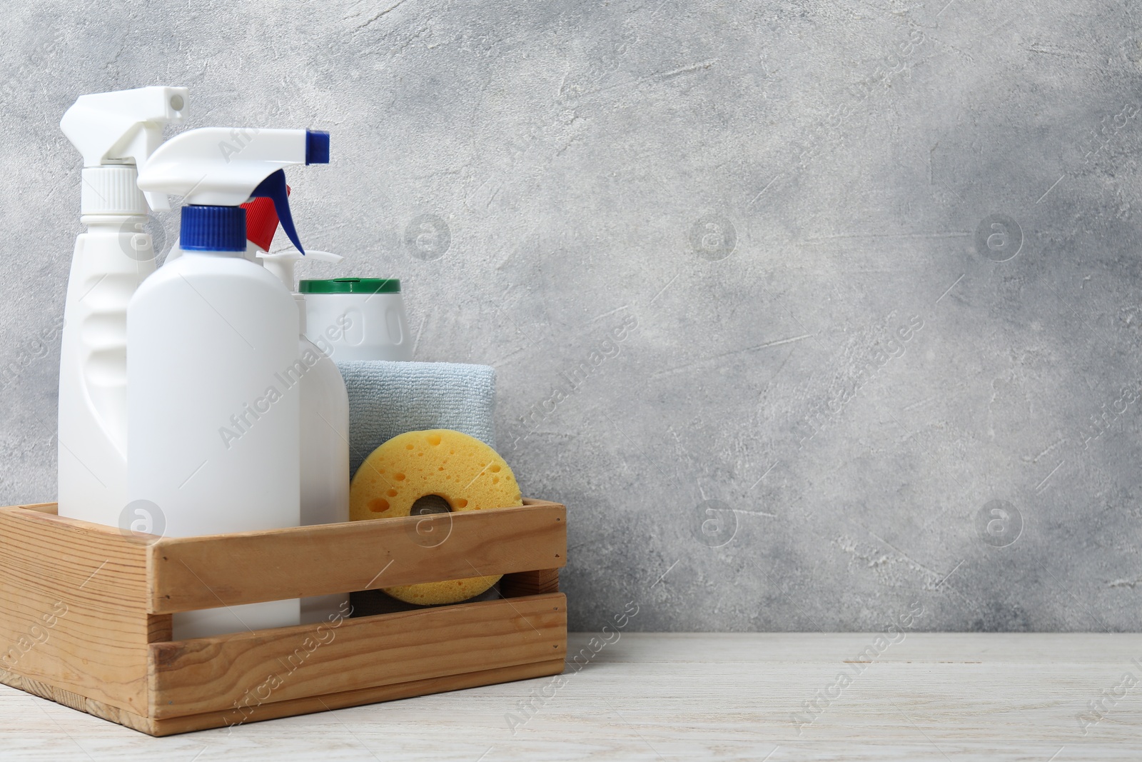 Photo of Eco-friendly cleaning products and supplies in crate on light wooden table, space for text