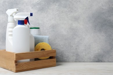 Photo of Eco-friendly cleaning products and supplies in crate on light wooden table, space for text