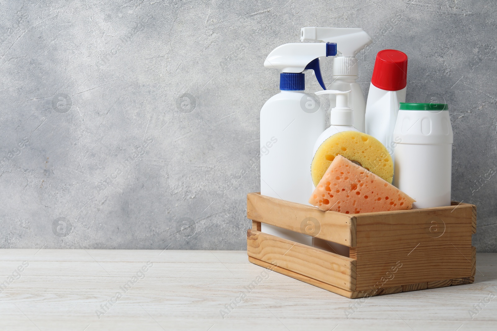 Photo of Eco-friendly cleaning products and supplies in crate on light wooden table, space for text