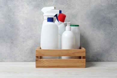 Photo of Different cleaning products in crate on light wooden table