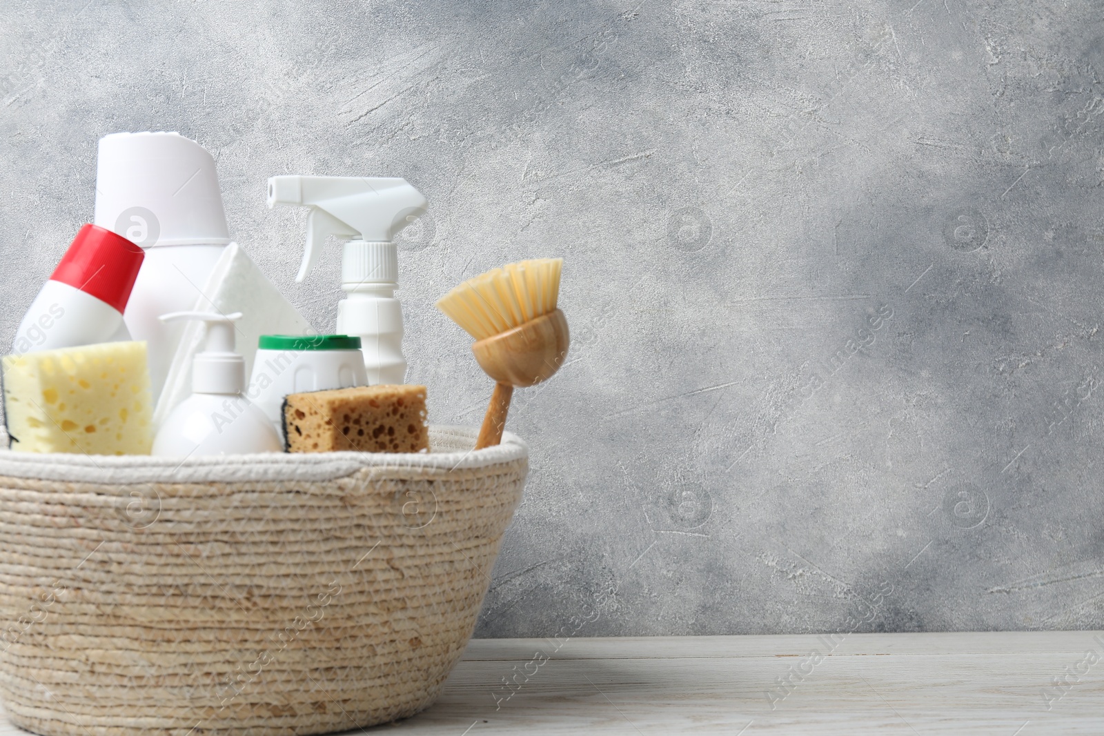 Photo of Eco-friendly cleaning products and supplies in wicker basket on light wooden table, space for text