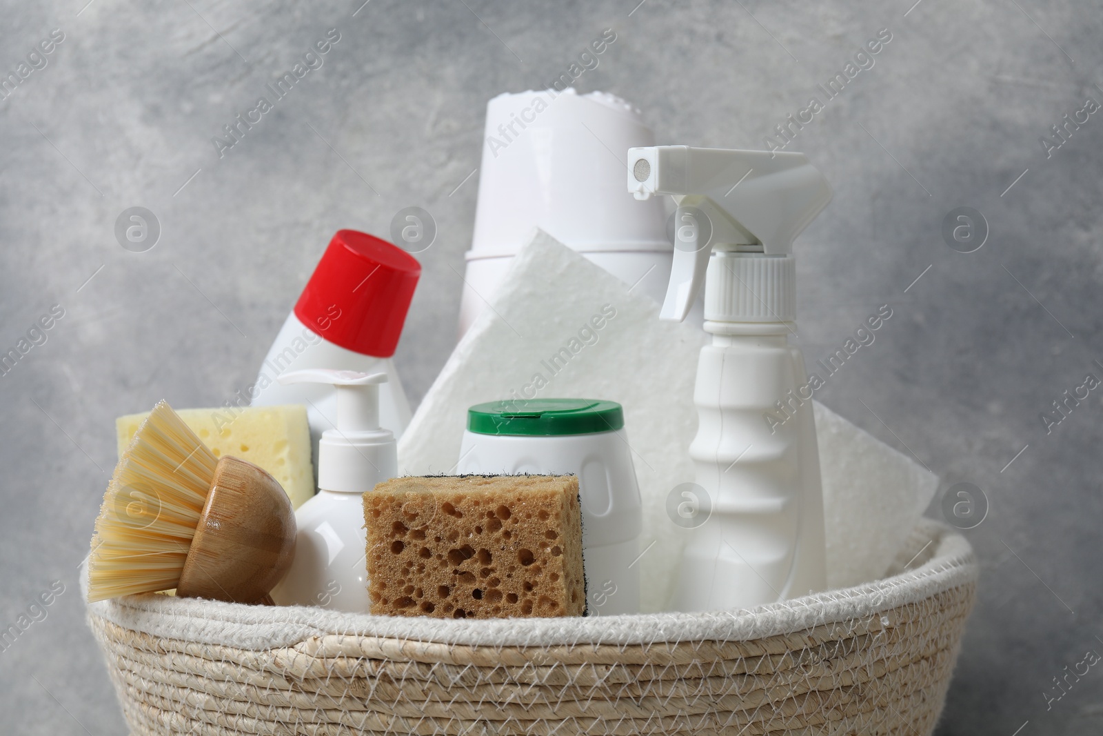 Photo of Eco-friendly cleaning products and supplies in wicker basket against grey background, closeup