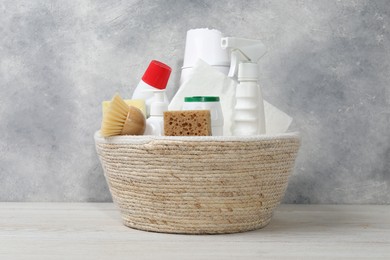 Photo of Eco-friendly cleaning products and supplies in wicker basket on light wooden table