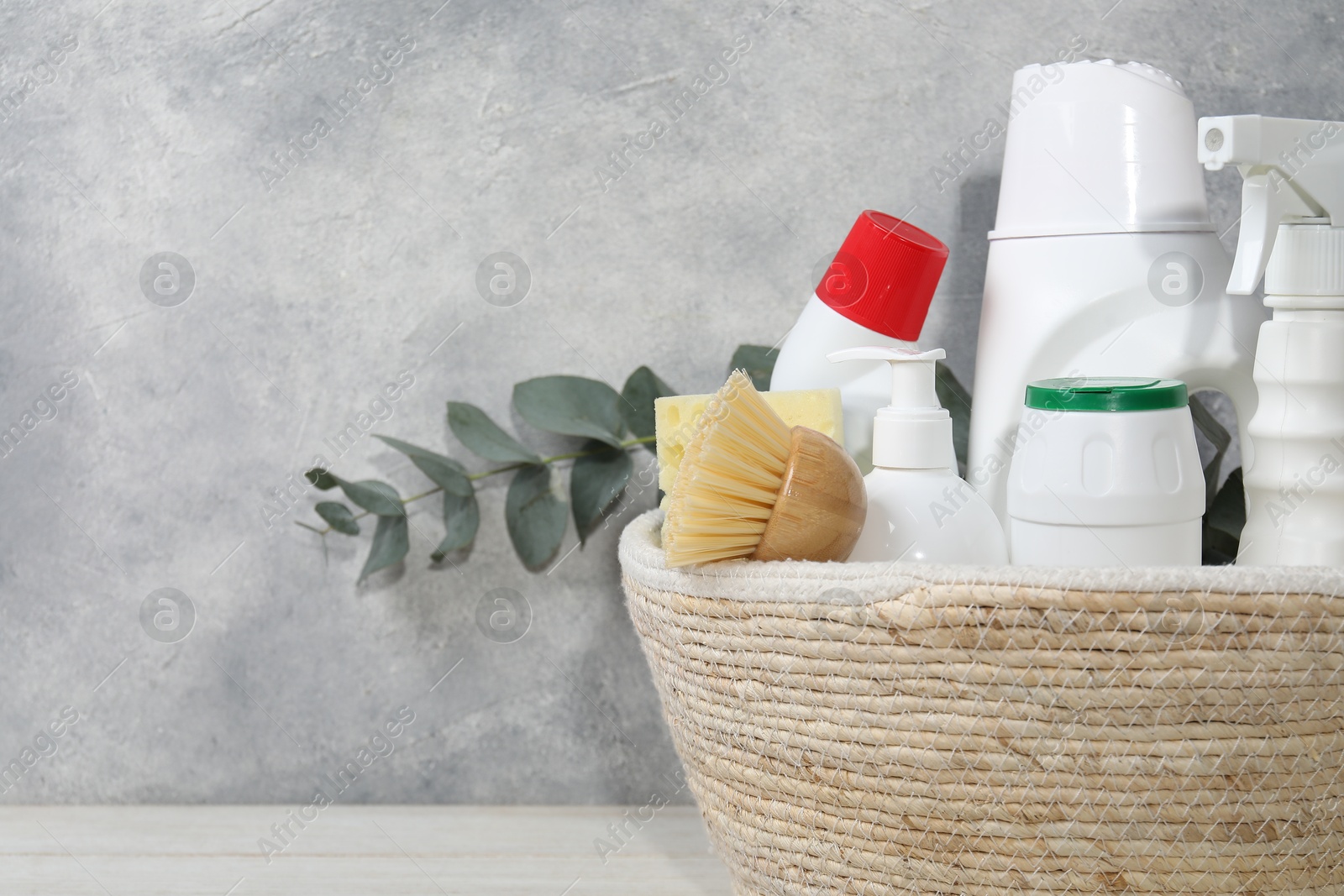 Photo of Eco-friendly cleaning products, supplies and eucalyptus branch in wicker basket on light wooden table, closeup. Space for text