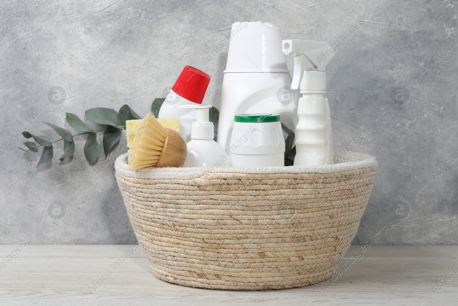 Photo of Eco-friendly cleaning products, supplies and eucalyptus branch in wicker basket on light wooden table