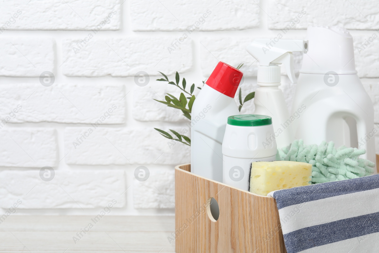 Photo of Eco-friendly cleaning products, supplies and green branches in crate on table against white brick wall, space for text