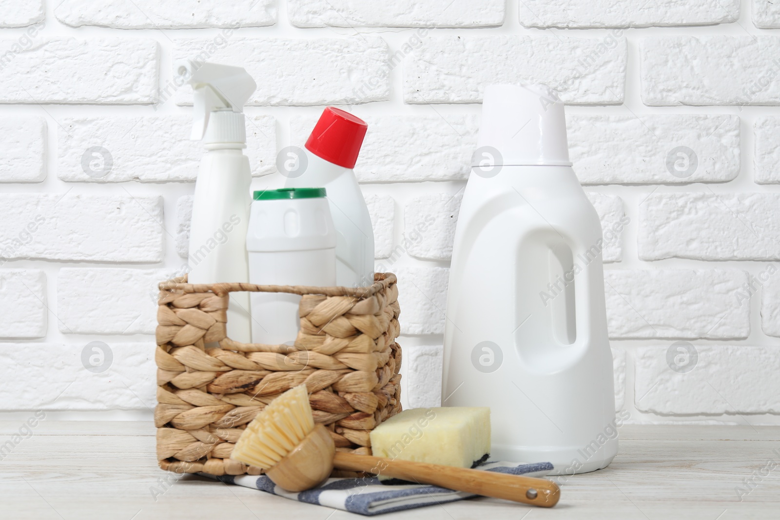 Photo of Eco-friendly cleaning products and supplies on light wooden table against white brick wall