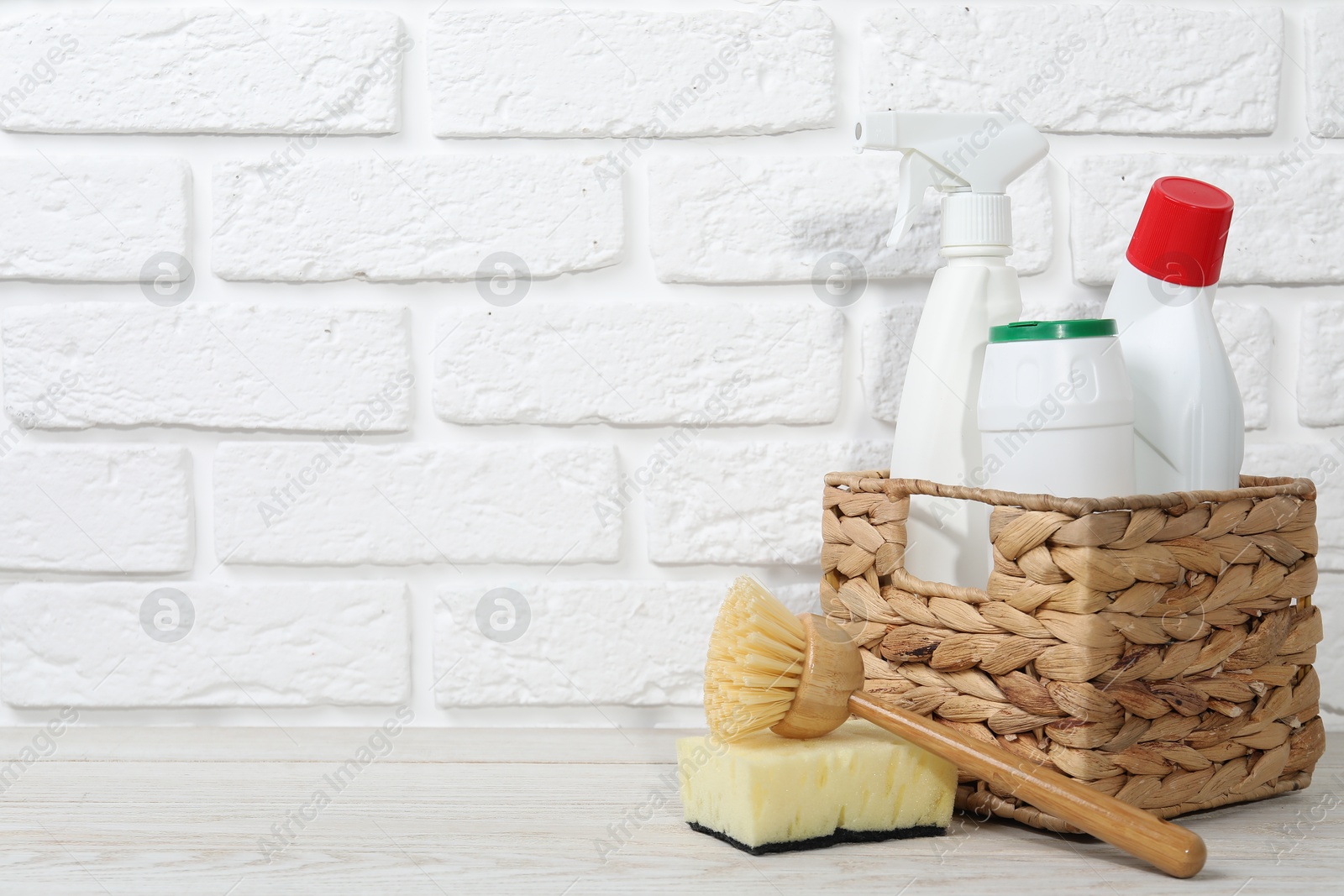 Photo of Eco-friendly cleaning products and supplies on light wooden table against white brick wall, space for text