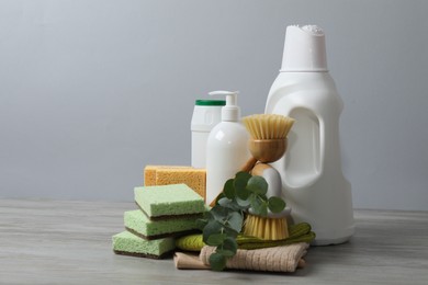 Photo of Eco-friendly cleaning products, supplies and eucalyptus branches on wooden table against grey background, space for text