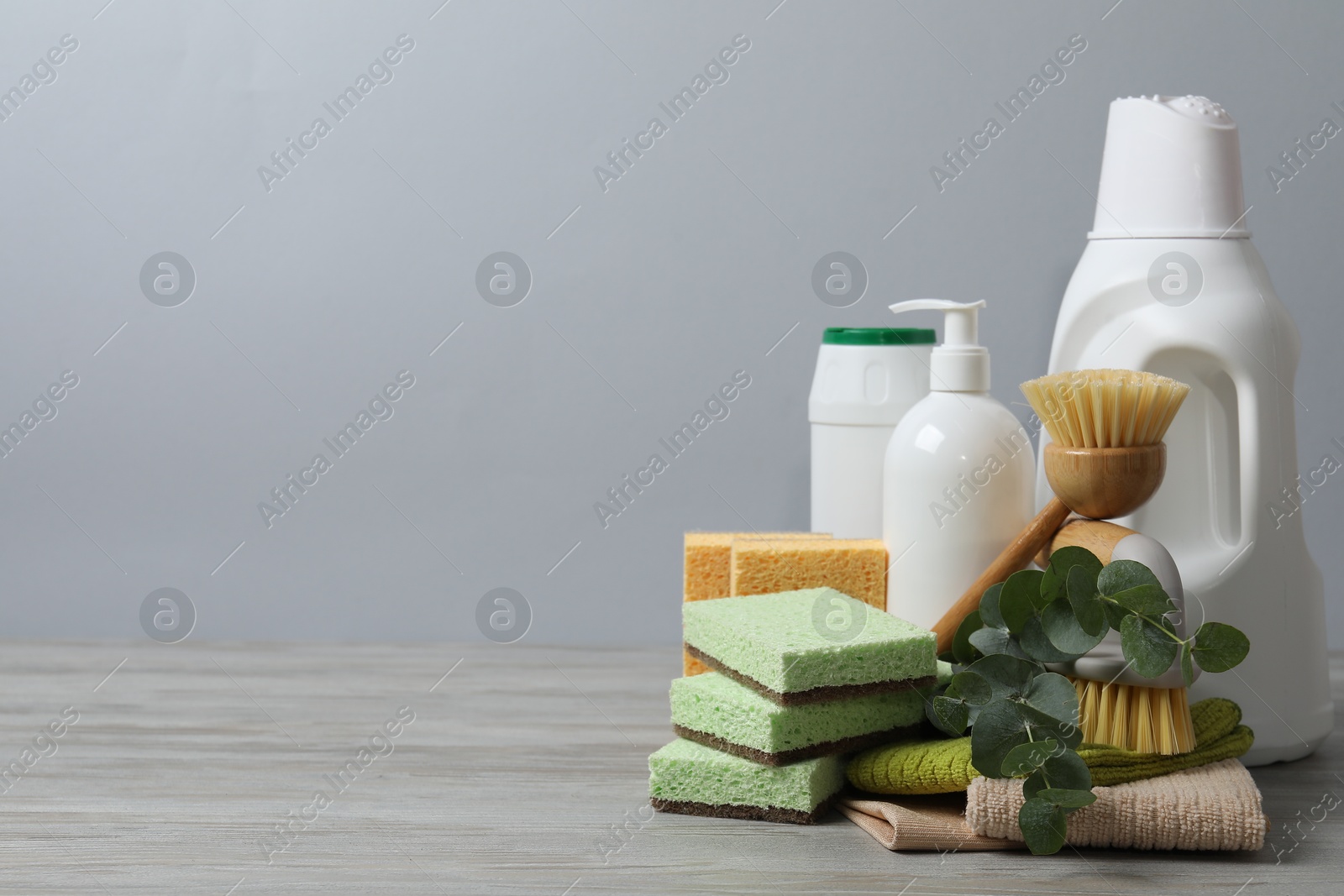 Photo of Eco-friendly cleaning products, supplies and eucalyptus branches on wooden table against grey background, space for text