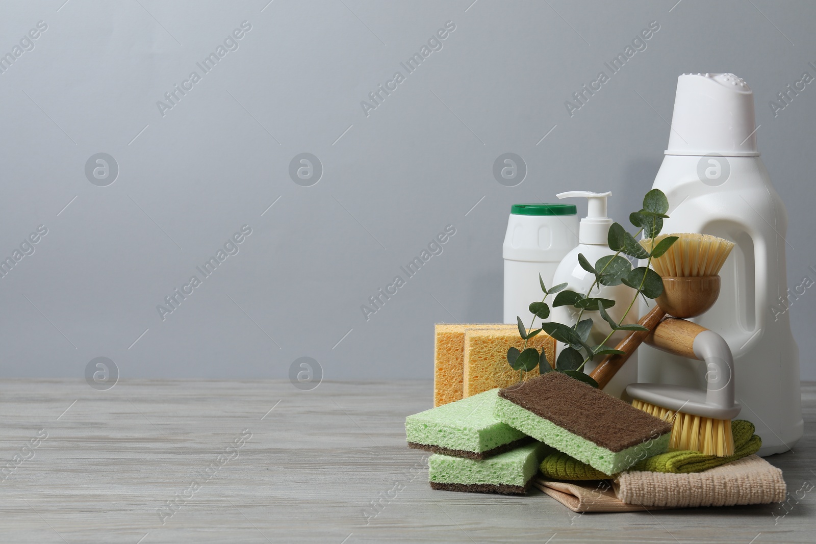 Photo of Eco-friendly cleaning products, supplies and eucalyptus branches on wooden table against grey background, space for text