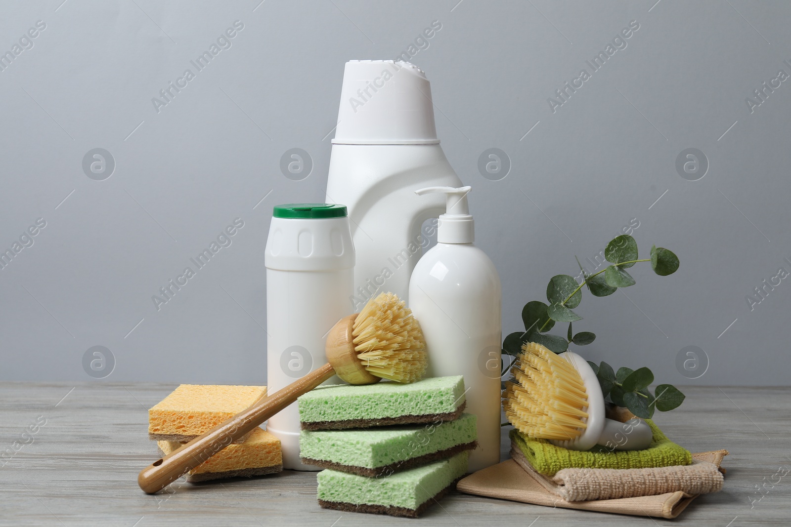 Photo of Eco-friendly cleaning products, supplies and eucalyptus branches on wooden table against grey background