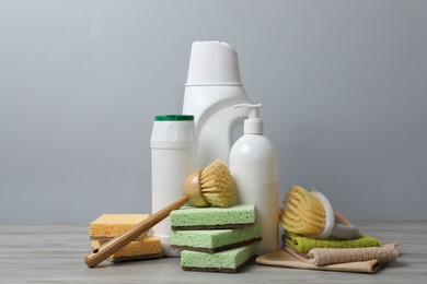 Photo of Eco-friendly cleaning products and supplies on wooden table against grey background