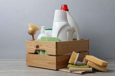 Photo of Eco-friendly cleaning products and supplies in crate on wooden table against grey background