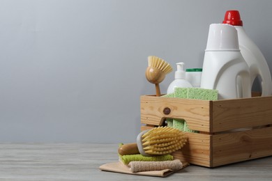 Photo of Eco-friendly cleaning products and supplies in crate on wooden table against grey background, space for text