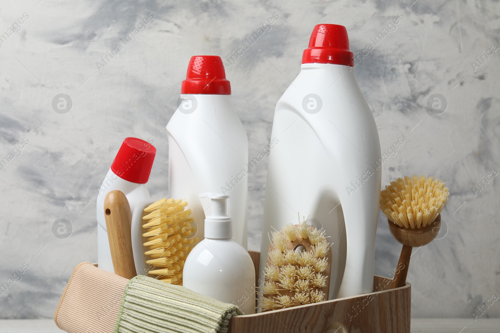 Photo of Different cleaning products and supplies in wooden crate against color background, closeup