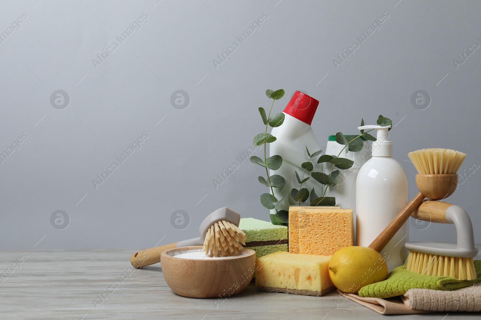 Photo of Eco-friendly cleaning products, supplies and eucalyptus branches on wooden table against grey background, space for text