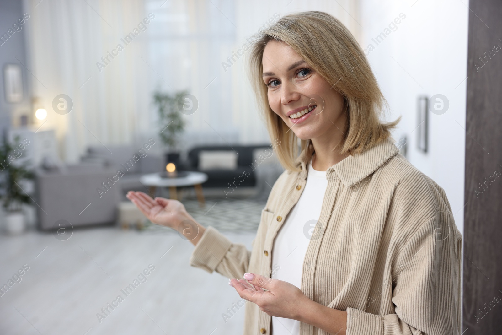 Photo of Cheerful woman welcoming guests to her apartment. Space for text