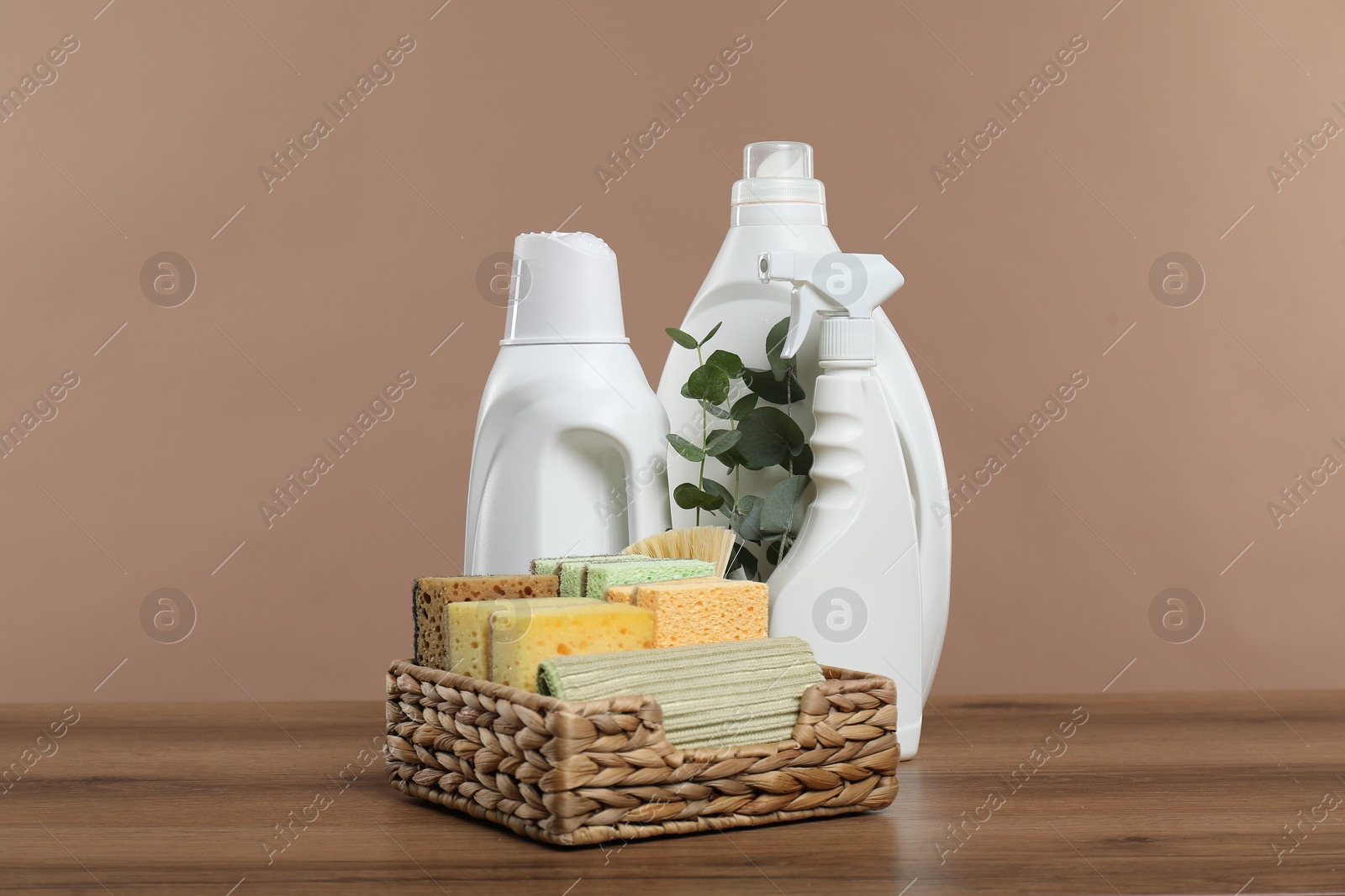 Photo of Eco-friendly cleaning products, supplies and eucalyptus branches on wooden table against beige background