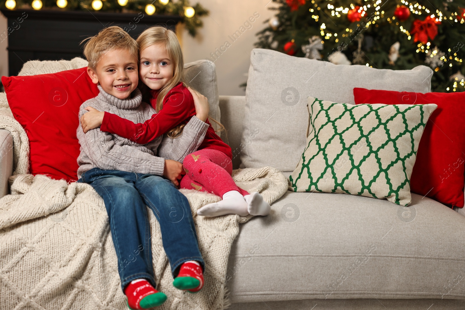 Photo of Little kids hugging on sofa in room decorated for Christmas