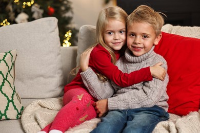 Little kids hugging on sofa in room decorated for Christmas