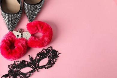 Photo of Fluffy handcuffs, lace mask and high-heeled shoes on pink background, flat lay. Space for text