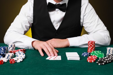 Professional croupier at gambling table with playing cards, casino chips and dice, closeup