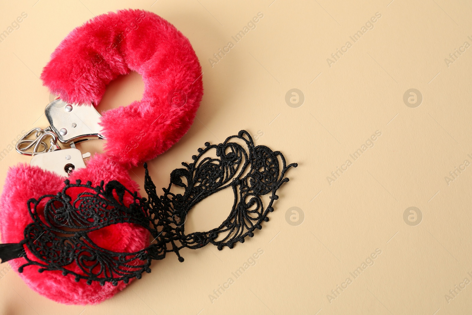 Photo of Pink fluffy handcuffs and lace mask on pale yellow background, flat lay. Space for text