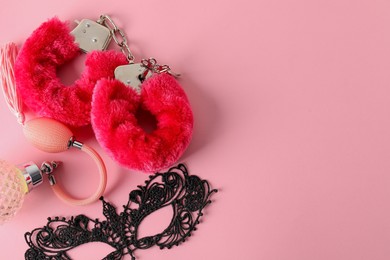 Photo of Fluffy handcuffs, lace mask and perfume bottle on pink background, flat lay. Space for text