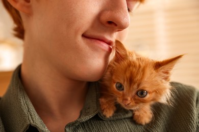 Photo of Teenage boy with his cute ginger kitten indoors, closeup