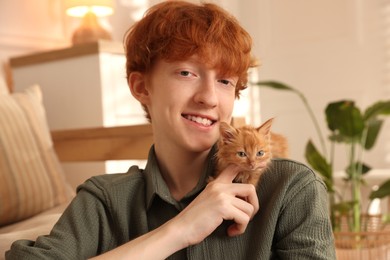 Photo of Redhead teenage boy with cute ginger kitten indoors